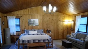 Ett rum med träpanel på väggarna, innehållande en säng, en soffa, ett nattduksbord, en lampa och en tavla.