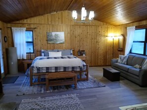 Ein Zimmer mit Holzwand, einem Bett, einem Schlafsofa, einem Nachttisch, einer Lampe und einem Bild an der Wand.