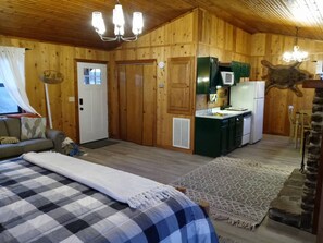 A cabin interior with a bed, kitchenette, and a stone fireplace. - Riverfront Eagle Cabin: Private Kings River Access, 15 Min to Eureka Springs (Berryville)