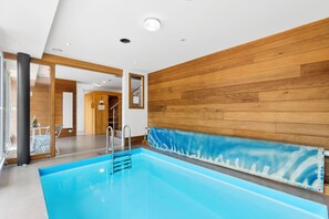 A modern indoor swimming pool with a wooden wall and a glass door leading to a hallway. - Luxurious villa with a pool, sauna, and garden, 15 minutes from Paris (Chatou)