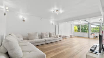 A spacious living room with a large sectional sofa, wooden flooring, and a television on a stand.