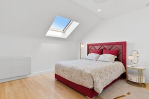 A bedroom with a skylight, a red headboard, a bedside table with a lamp, and a wooden floor. - Luxurious villa with a pool, sauna, and garden, 15 minutes from Paris (Chatou)