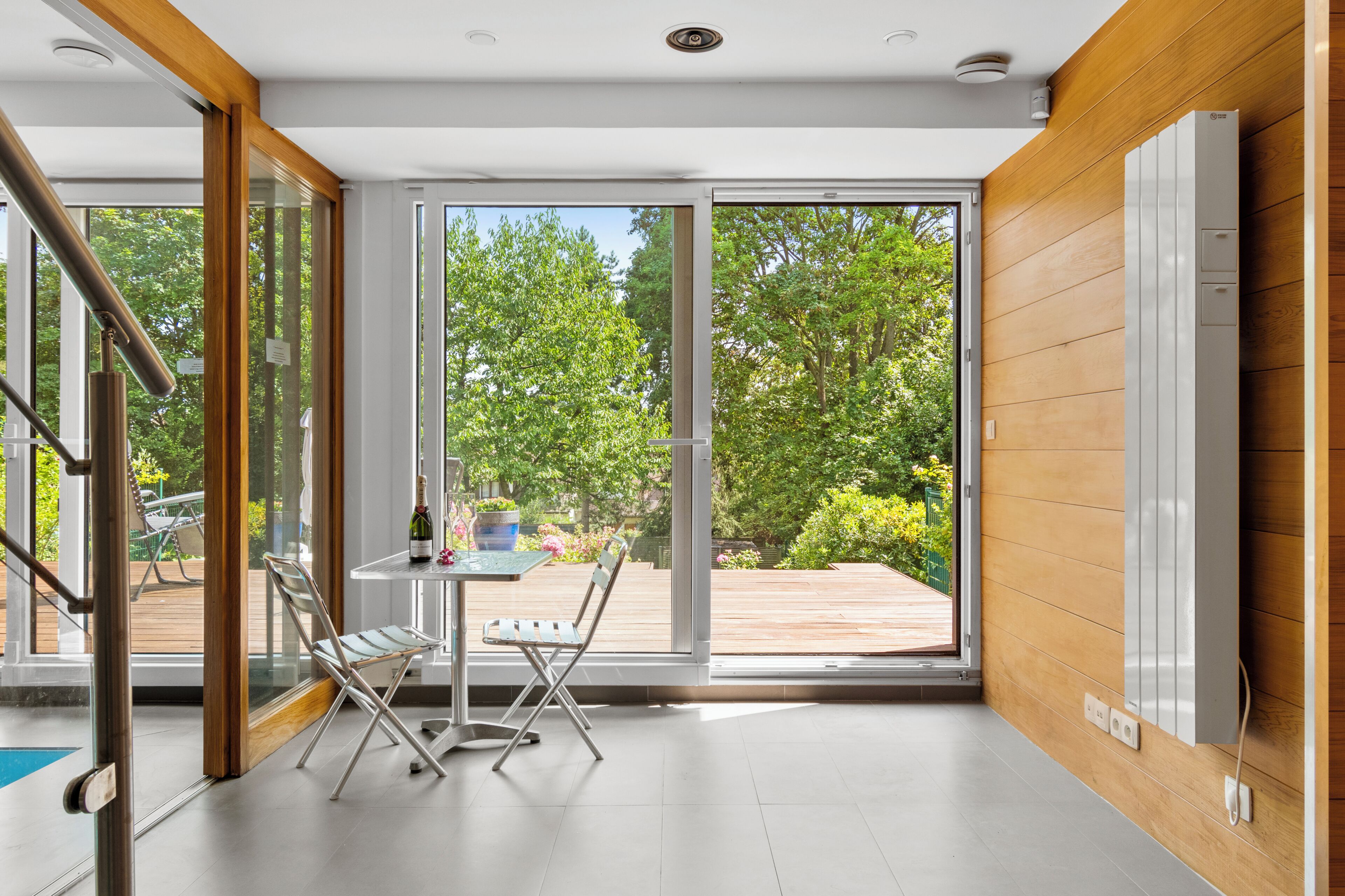 Decoração moderna com porta de vidro que dá para um deck externo, uma mesa pequena com cadeiras e uma parede de madeira com termostato.