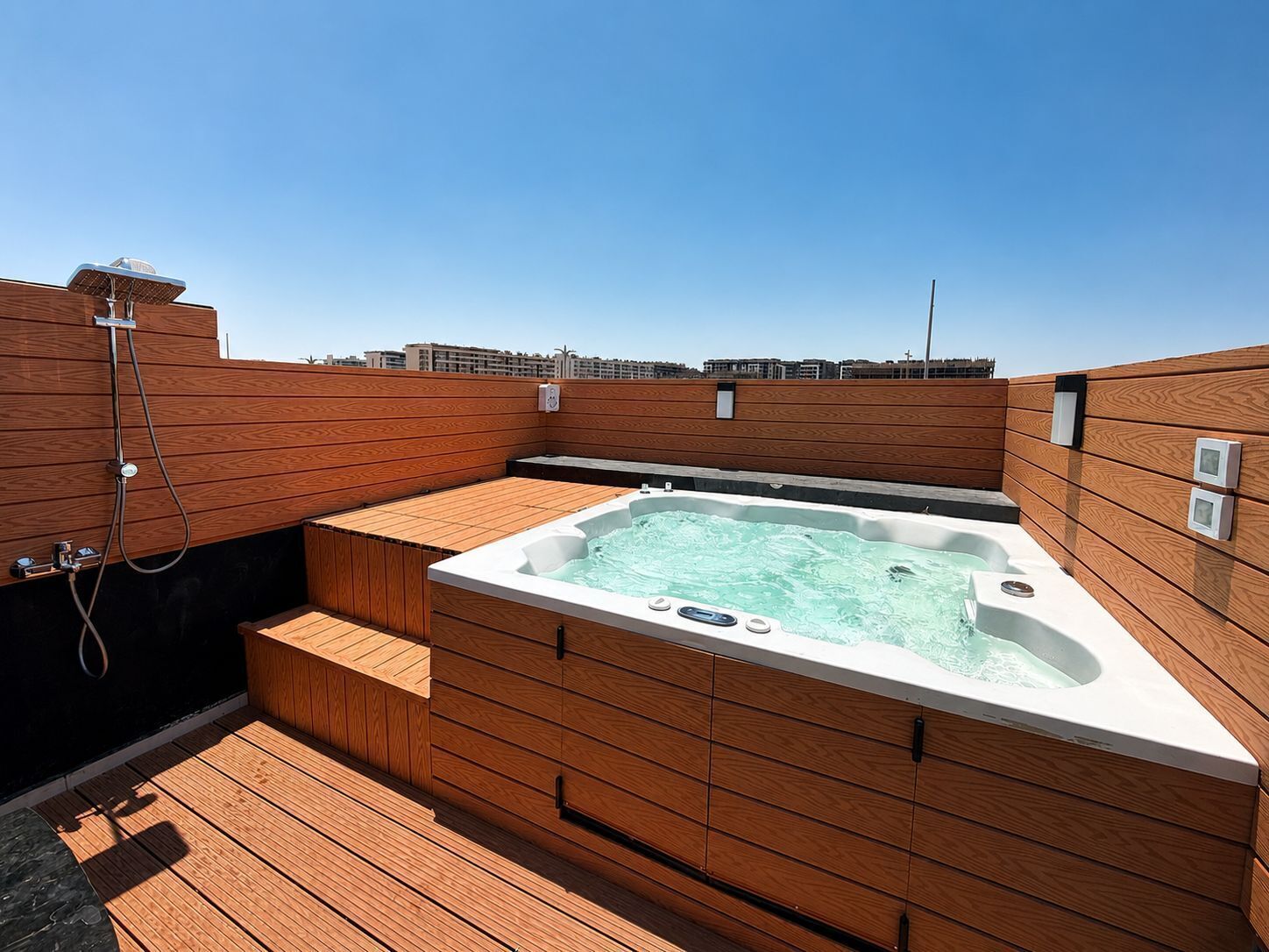 Uma banheira de hidromassagem no terraço, com painéis de madeira e vista clara do horizonte da cidade ao fundo.