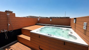 Uma banheira de hidromassagem no terraço, com painéis de madeira e vista clara do horizonte da cidade ao fundo.