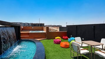Piscina no terraço com cachoeira, rodeada por grama sintética verde e espreguiçadeiras coloridas.