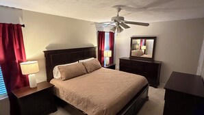 A bedroom with a bed, nightstands, a ceiling fan, a mirror, and red curtains.