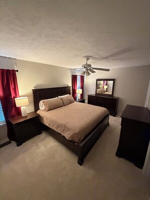 A bedroom with a bed, nightstands, a ceiling fan, a mirror, and red curtains.