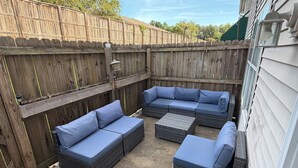 An outdoor patio with a sectional sofa and a small table, enclosed by a wooden fence.