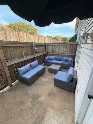 An outdoor patio with a sectional sofa and a small table, enclosed by a wooden fence.