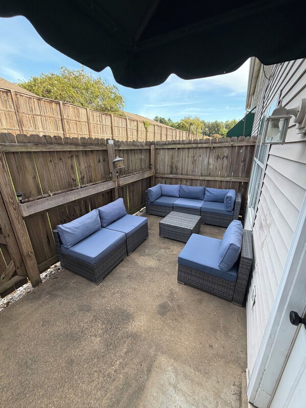 Un patio exterior con un sofá seccional y una mesa pequeña, delimitado por una valla de madera.