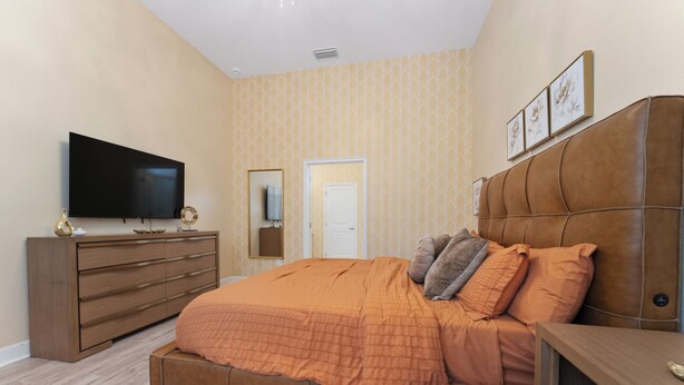 A bedroom with a bed, a dresser, a television, a door, and a wall with framed pictures. - NEW Luxury 14BR Estate - Sleeps 36 - Theater/Games (Davenport)