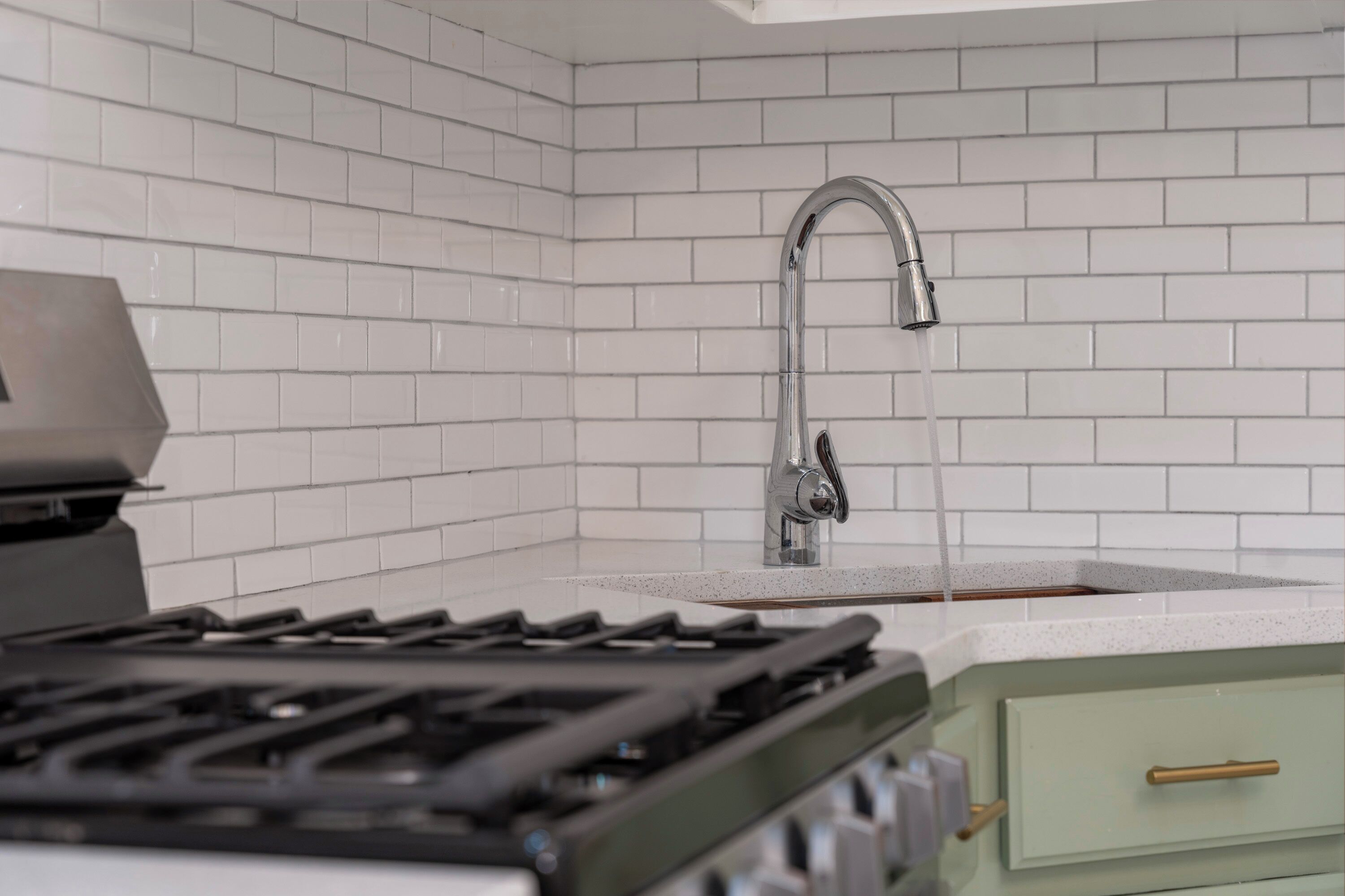 A kitchen with white tiled walls, a stainless steel faucet, a gas stove, and a green cabinet.