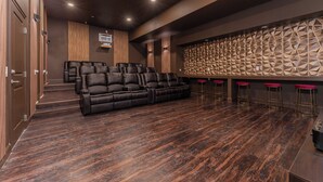 A modern home theater with a large sectional sofa, a wall-mounted speaker system, and a patterned acoustic panel. - NEW Luxury 14BR Estate - Sleeps 36 - Theater/Games (Davenport)