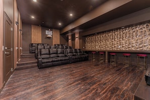 A modern home theater with a large sectional sofa, a wall-mounted speaker system, and a patterned acoustic panel. - NEW Luxury 14BR Estate - Sleeps 36 - Theater/Games (Davenport)