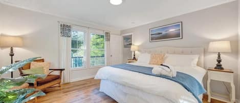 A bedroom with a large bed, two bedside tables with lamps, a chair, and a window with curtains.