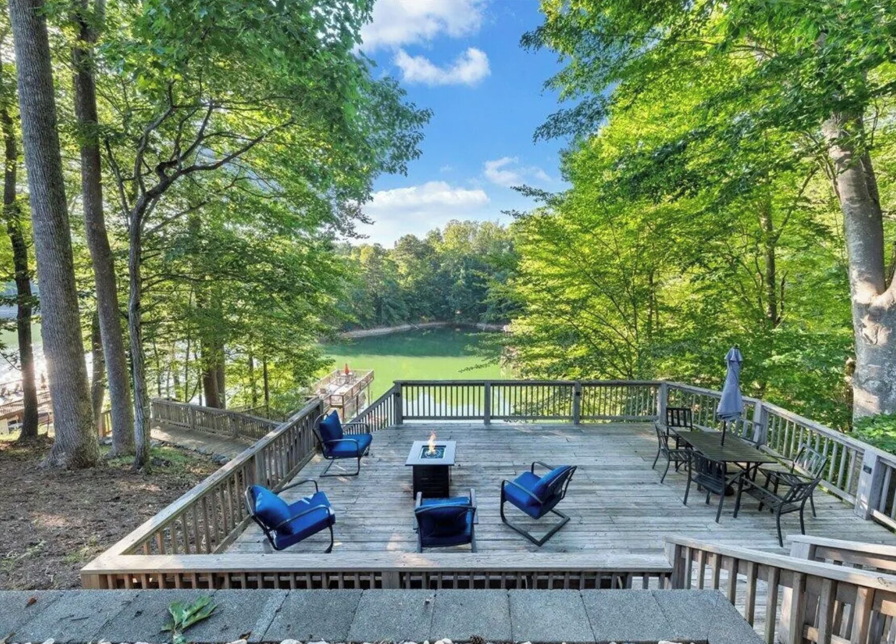 A deck with outdoor furniture and a view of a lake surrounded by trees.