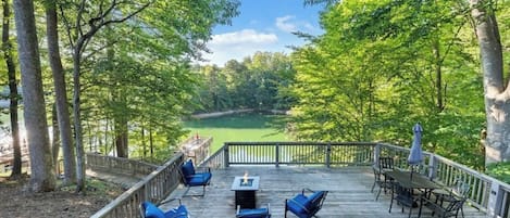 A deck with outdoor furniture and a view of a lake surrounded by trees.