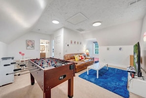 A spacious room with a foosball table, a blue rug, a brown leather sofa, and a television. - Sweetwater Cove:  3-Level Lakefront Retreat (Moneta)