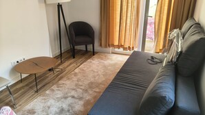 A room with a sofa, a chair, a small table, and a lamp. - Large and cozy apartment. Next to the António Borges Garden and Shopping Center (Ponta Delgada)