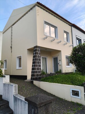 A two-story building with a beige facade, a stone pillar, and a small garden area with steps leading up to the entrance. - Cozy Premium I - Spacious, comfortable, welcoming (Ponta Delgada)