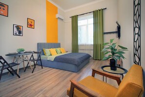 A modern bedroom with a bed, a desk, and a chair. There is a television mounted on the wall and a window with curtains. - Leon, Metro Raiymbek, 15 min to Arbat (Almaty)