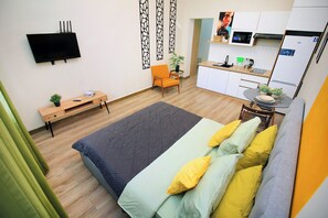 Una habitación pequeña con cama, escritorio, silla y kitchenette.