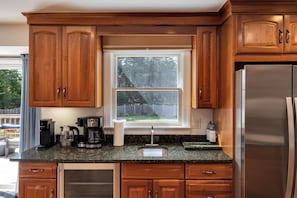 A kitchen with wooden cabinets, a stainless steel refrigerator, a coffee maker, and a window with a view of the outdoors.