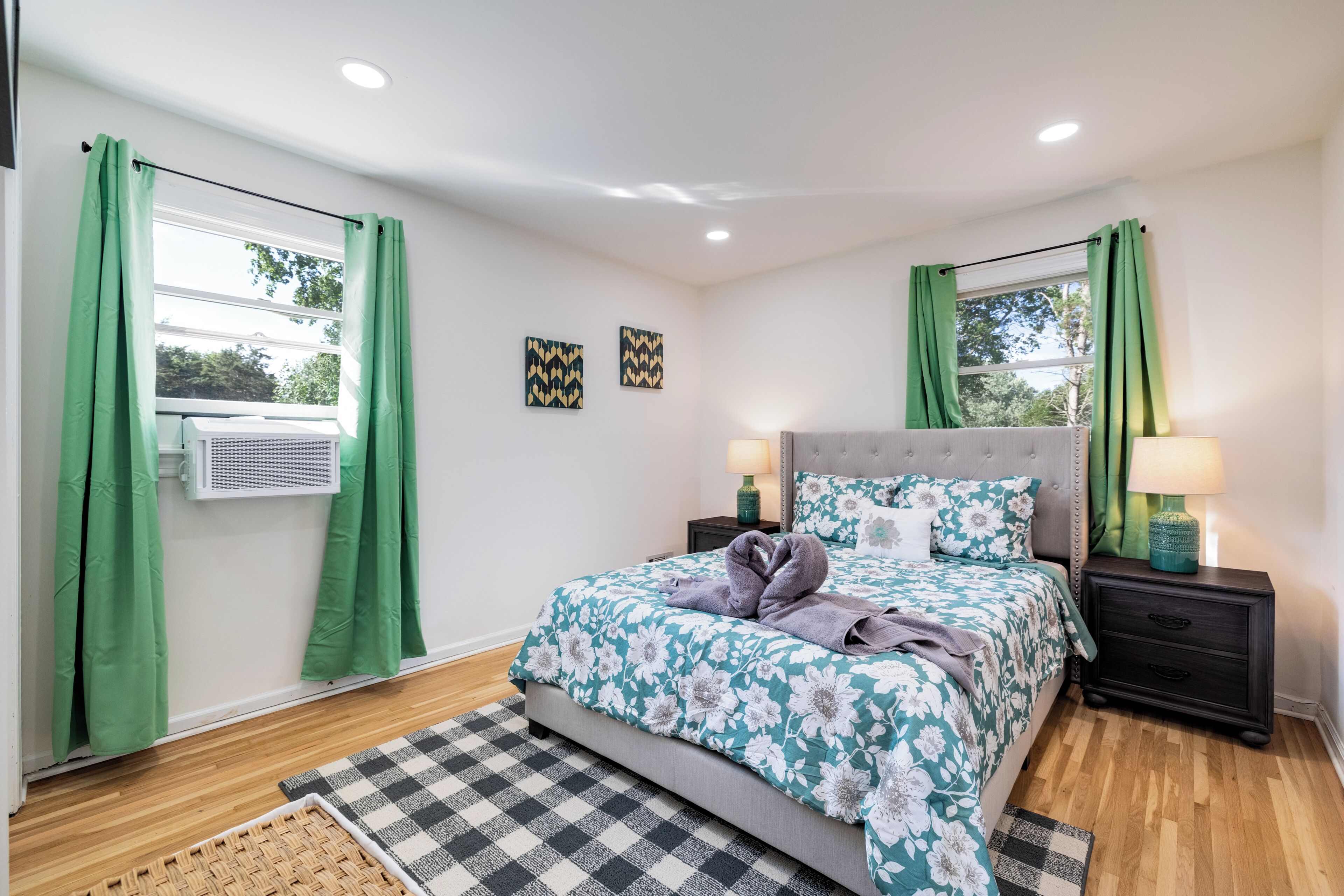 Un dormitorio con cama, dos lámparas de noche, una ventana con cortinas, un aire acondicionado de pared y un tapete a cuadros.