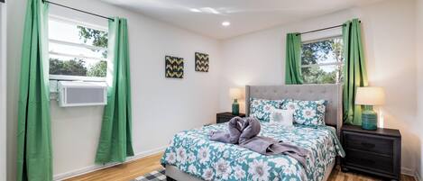 Un dormitorio con cama, dos lámparas de noche, una ventana con cortinas, un aire acondicionado de pared y un tapete a cuadros.