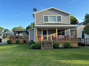 Une maison à deux étages avec un porche, une antenne parabolique et un drapeau.