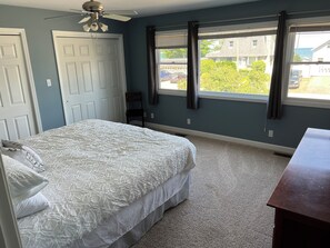 Une chambre à coucher avec un lit, un ventilateur de plafond, une fenêtre avec des rideaux et une vue sur l’extérieur.