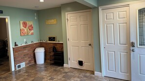 A hallway with a white door, a brick wall, a trash can, and a shelf with decorative items. - Marvelous 4-bedroom house with AC in charming Port Austin (Port Austin)