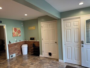 A hallway with a white door, a brick wall, a trash can, and a shelf with decorative items. - Marvelous 4-bedroom house with AC in charming Port Austin (Port Austin)