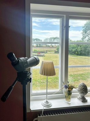 A room with a telescope on a tripod, a lamp, and a window with a view of a grassy field. - Farmhouse with view towards Kullaberg (BÅSTAD)