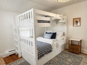 Ein Stockbett mit unterem Bett, ein kleiner Nachttisch und ein gemustertes Teppich.