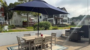 An outdoor patio with a table and chairs, a barbecue grill, and a large umbrella providing shade.