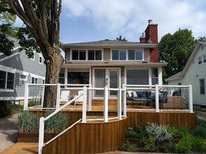 A two-story house with a deck, a chimney, and a large tree. - Lakefront Retreat w/ 100' Private Dock - LEEHAVEN on Spring Lake (Spring Lake)