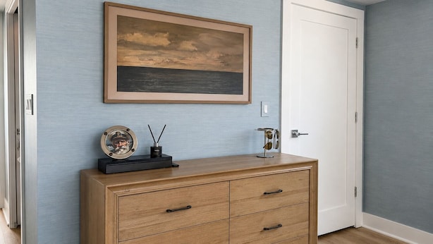 A room with a wooden cabinet, a framed painting, and a white door.