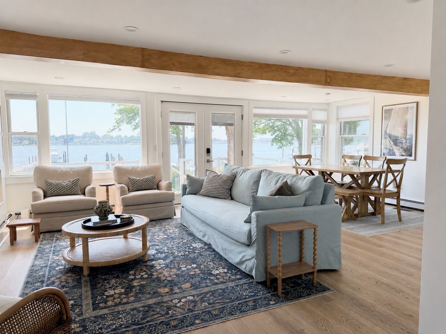 A spacious living room with a large window overlooking a body of water, a cozy seating area with a sofa and armchairs, and a dining table with chairs.