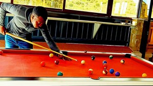 A pool table with balls, a person playing, and a window with a view. - Aqua Resort Naivasha (Naivasha)