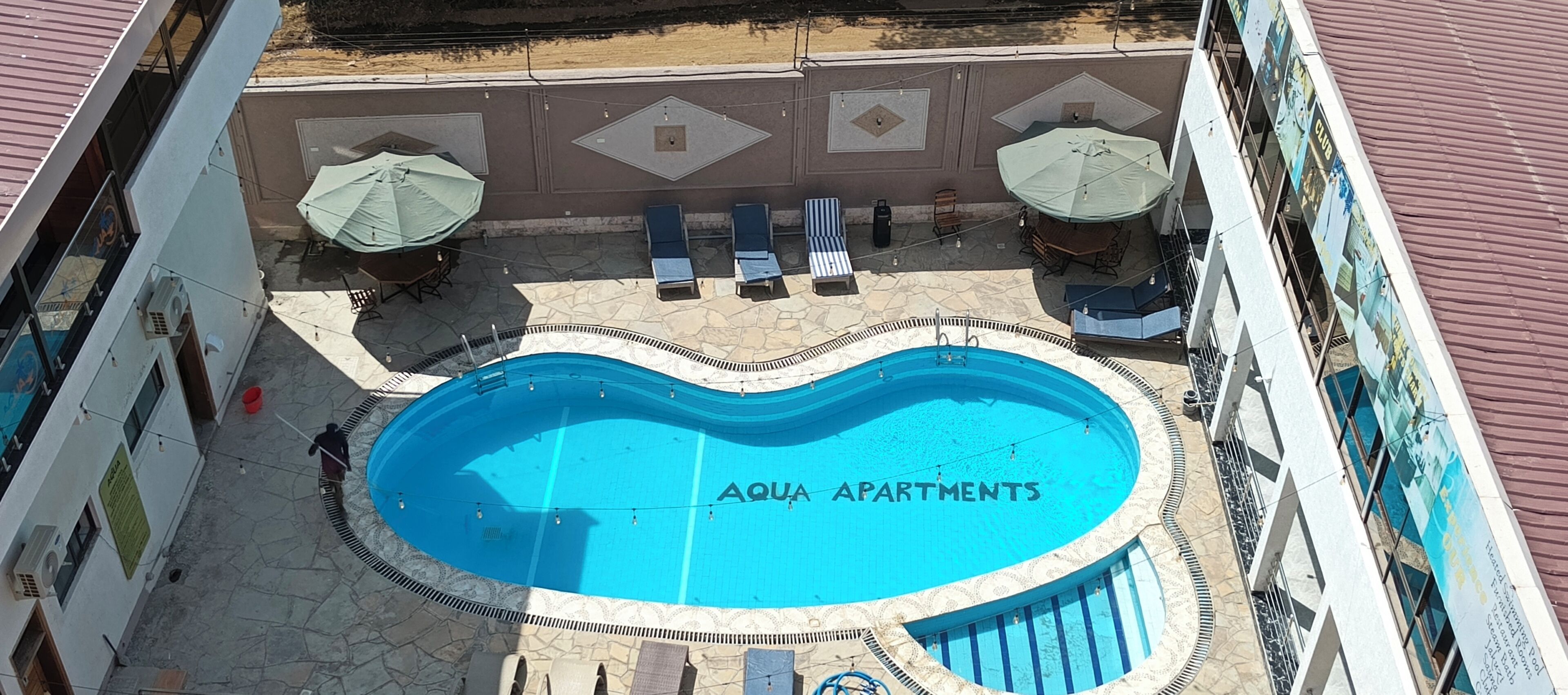 Piscina com espreguiçadeiras e guarda-sóis, em um deck revestido com azulejos.