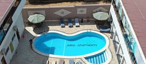 Ein Swimmingpool mit Liegestühlen und Sonnenschirmen, umgeben von einer gefliesten Liegefläche.