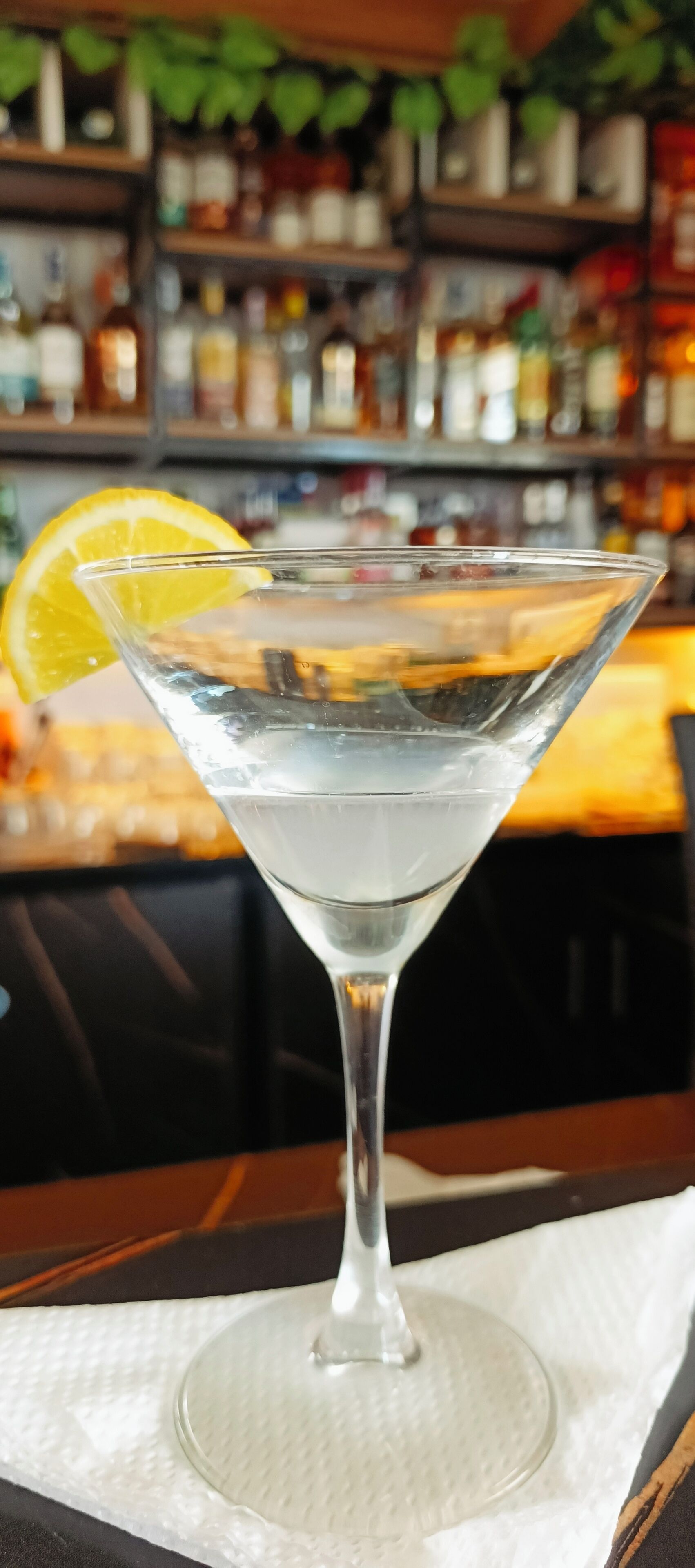 A clear glass martini glass with a lemon slice on the rim, placed on a white napkin.