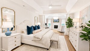 A bedroom with a large bed, bedside tables, a dresser, a mirror, and a fireplace in the background. - Exclusive Masters Retreat — Just Minutes from Augusta National (North Augusta)