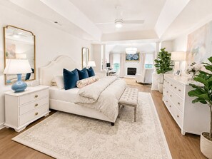 A bedroom with a large bed, bedside tables, a dresser, a mirror, and a fireplace in the background. - Exclusive Masters Retreat — Just Minutes from Augusta National (North Augusta)