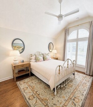 Une chambre à coucher comprenant un lit, des tables de chevet, un ventilateur de plafond, une fenêtre avec des rideaux et un tapis.