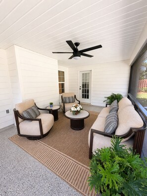 Un patio couvert avec un ventilateur de plafond, des meubles pour s’asseoir et une vue sur l’extérieur.