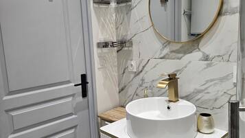 A bathroom with a white door, a round mirror with a gold frame, a white sink with a gold faucet, and a marble wall.