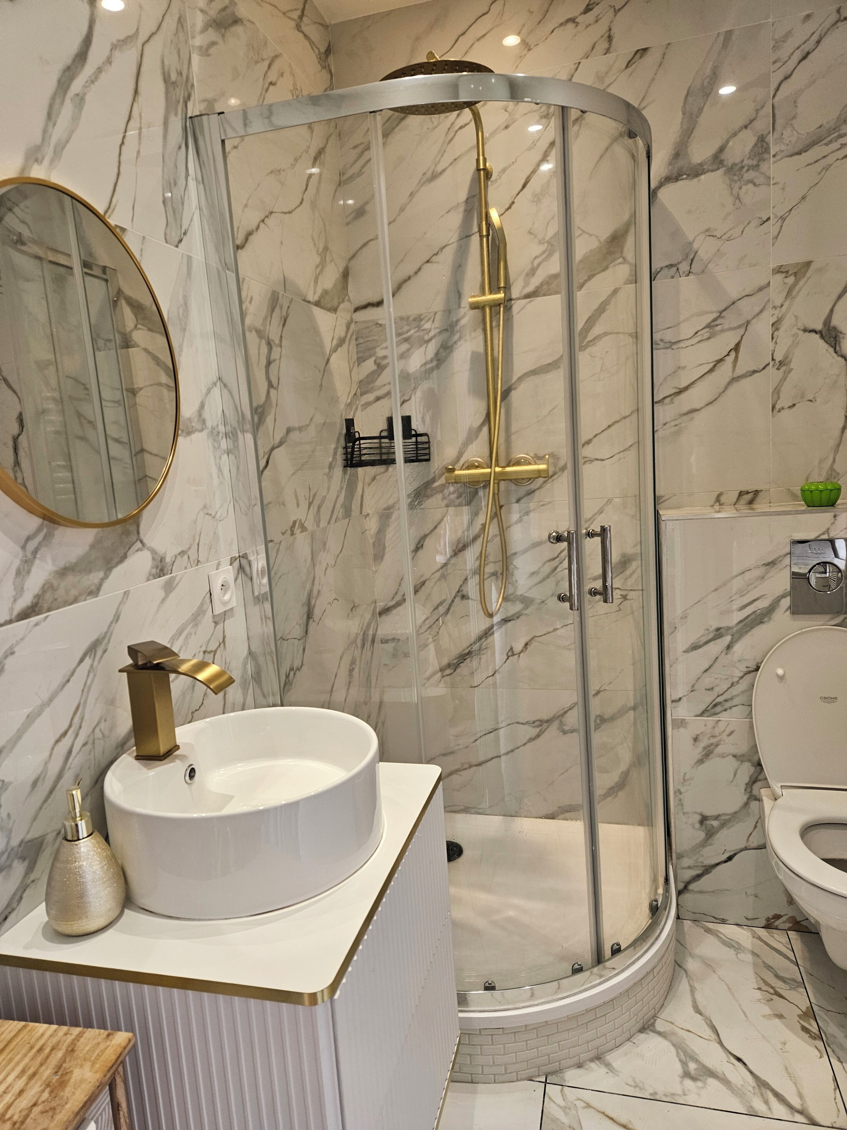 Un baño moderno con cabina de ducha de vidrio curvo, un lavabo redondo con grifo dorado y un inodoro.